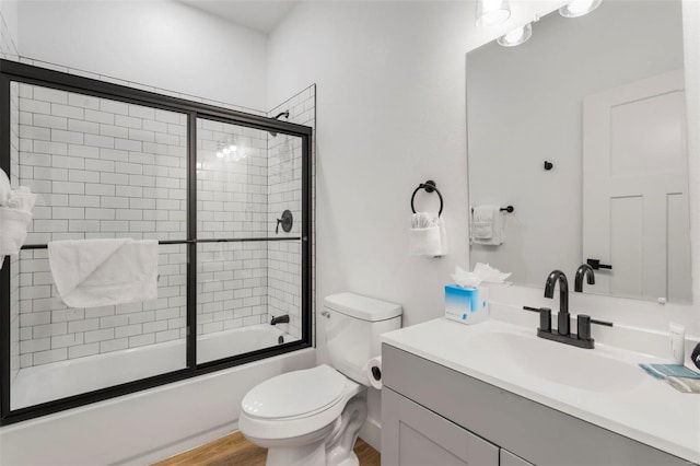 full bathroom with shower / bath combination with glass door, vanity, hardwood / wood-style flooring, and toilet