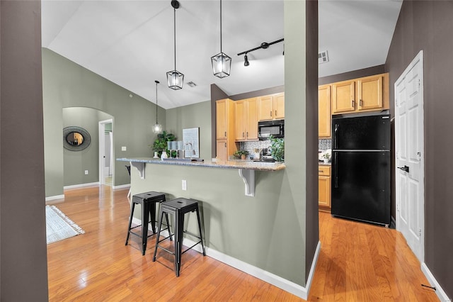 kitchen with pendant lighting, light brown cabinets, black appliances, decorative backsplash, and a kitchen bar