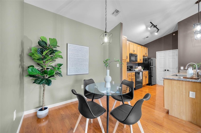 dining space with light hardwood / wood-style flooring, vaulted ceiling, and sink