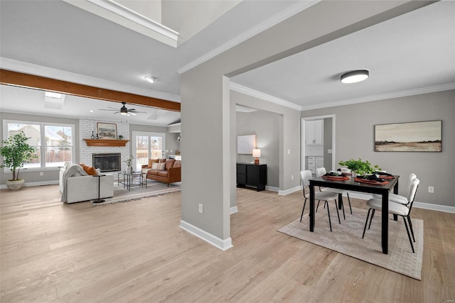 dining room featuring crown molding, a fireplace, ceiling fan, and light wood-type flooring