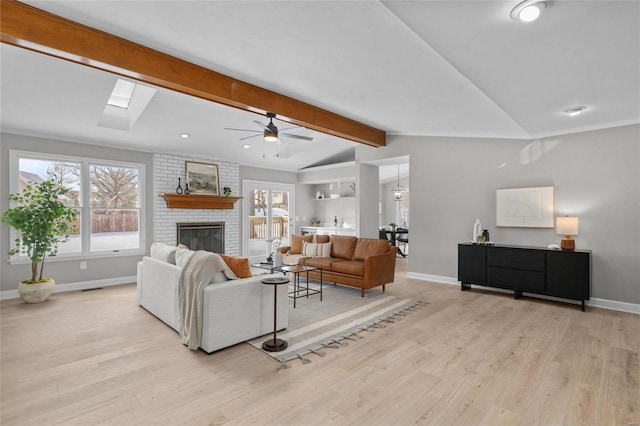 living room with a fireplace, lofted ceiling with skylight, light hardwood / wood-style flooring, and ceiling fan