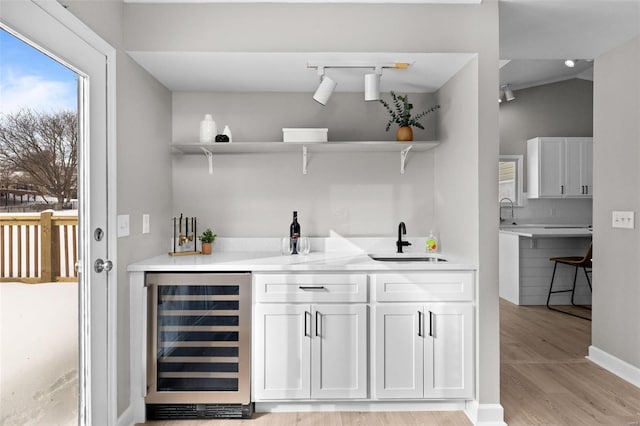 bar featuring backsplash, beverage cooler, sink, light hardwood / wood-style flooring, and white cabinetry