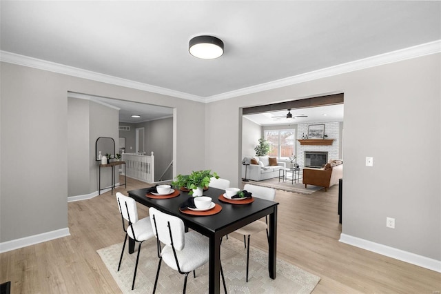 dining area featuring a brick fireplace, crown molding, ceiling fan, and light wood-type flooring