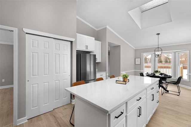 kitchen featuring white cabinetry, a center island, stainless steel fridge, lofted ceiling with skylight, and a kitchen bar