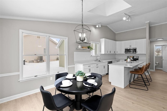 dining room with lofted ceiling with skylight, an inviting chandelier, crown molding, sink, and light hardwood / wood-style floors