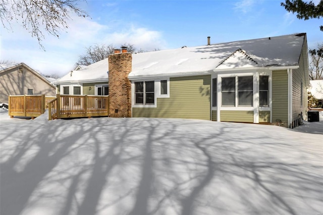 snow covered back of property with cooling unit and a wooden deck