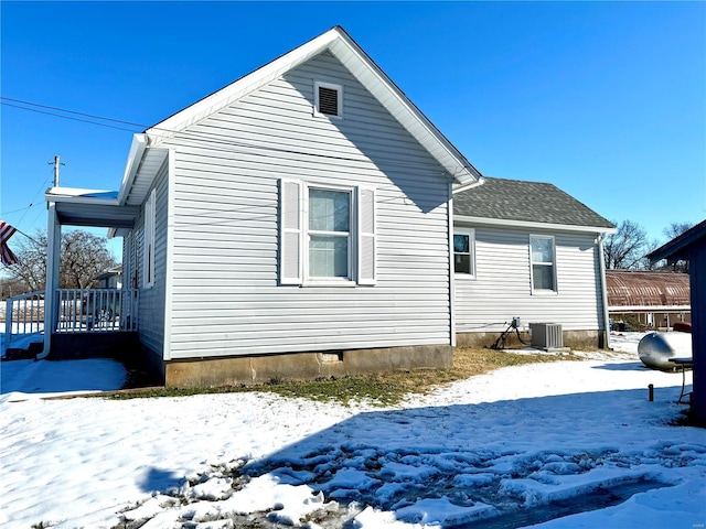 snow covered rear of property featuring central AC