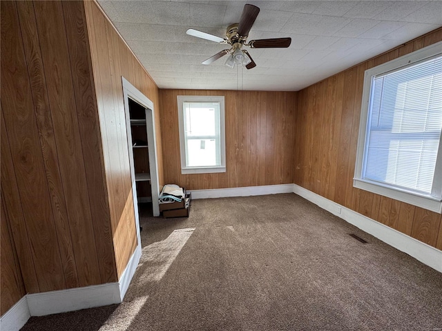 interior space with ceiling fan, carpet floors, and wood walls