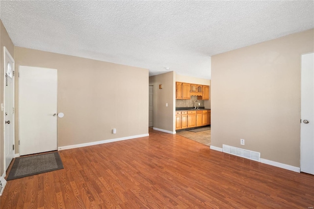 spare room featuring sink, light hardwood / wood-style flooring, and a textured ceiling