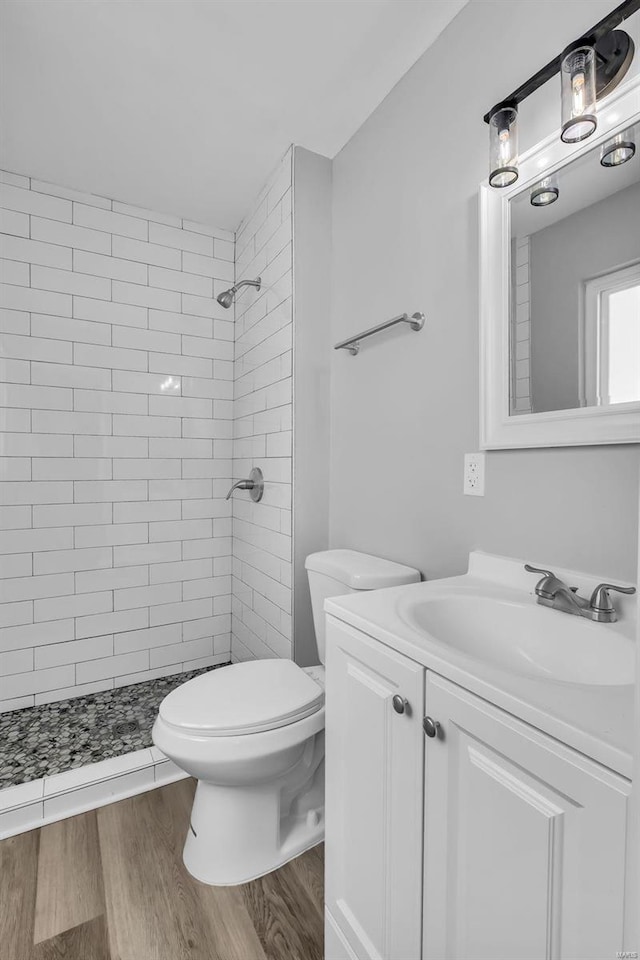 bathroom with hardwood / wood-style floors, vanity, toilet, and a tile shower