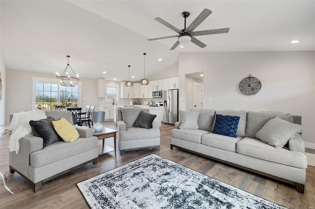 living room with hardwood / wood-style floors, ceiling fan with notable chandelier, vaulted ceiling, and sink