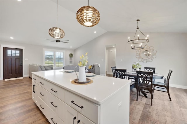 kitchen featuring ceiling fan with notable chandelier, decorative light fixtures, light hardwood / wood-style flooring, a center island, and white cabinetry