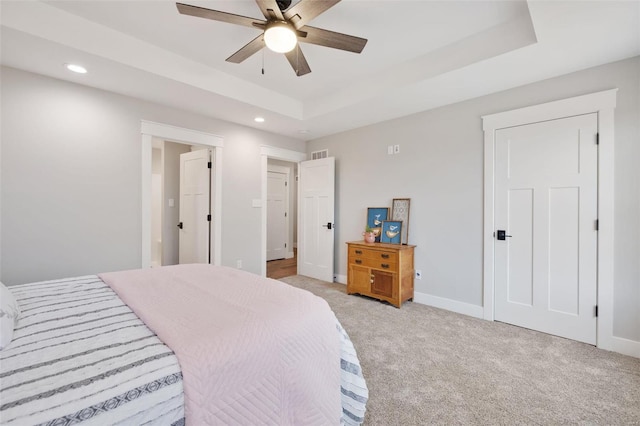 bedroom featuring light colored carpet, a raised ceiling, and ceiling fan