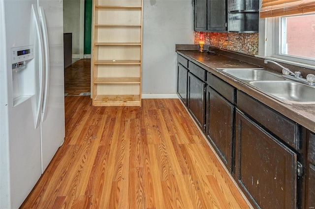 kitchen featuring white refrigerator with ice dispenser, decorative backsplash, light wood-type flooring, and sink