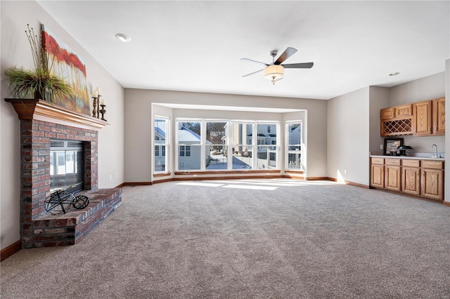 unfurnished living room featuring a brick fireplace, carpet floors, ceiling fan, and wet bar