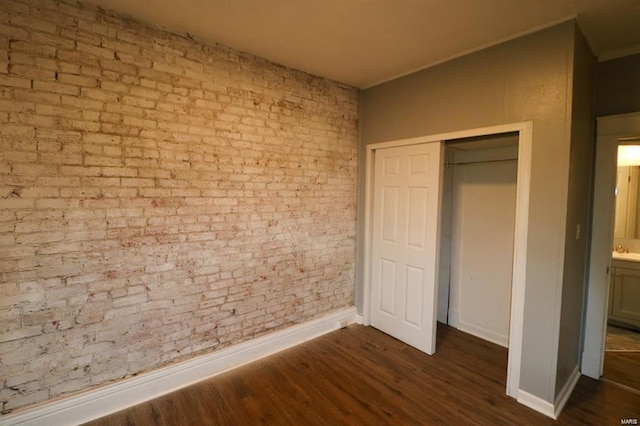 unfurnished bedroom featuring a closet, dark wood-type flooring, and brick wall