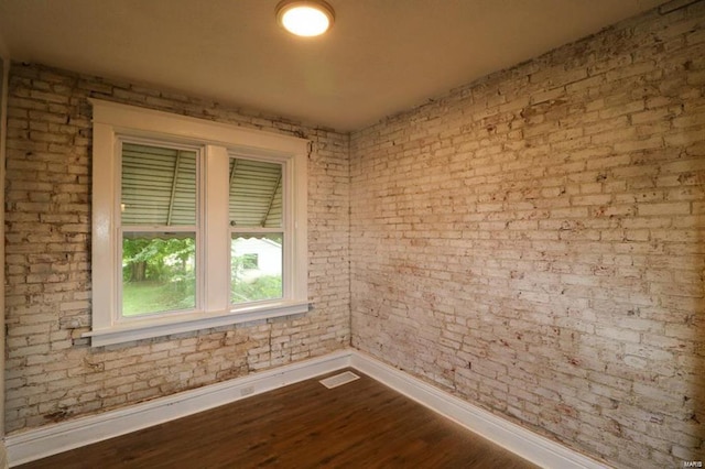 empty room featuring hardwood / wood-style floors and brick wall