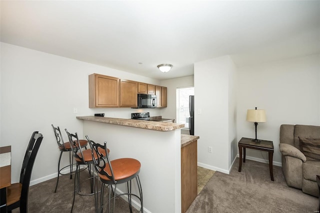 kitchen featuring black appliances, dark carpet, kitchen peninsula, and a breakfast bar area