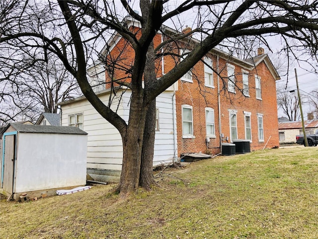 back of property with central air condition unit, a yard, and a shed