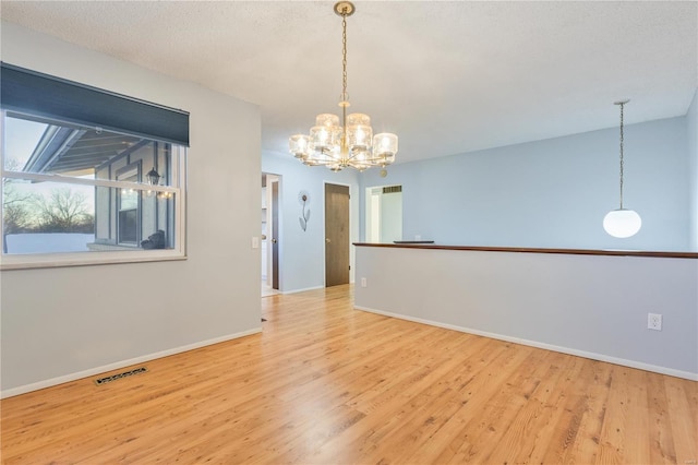 spare room featuring a textured ceiling, a notable chandelier, and light wood-type flooring