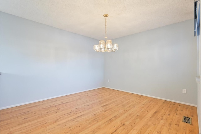 spare room with a textured ceiling, an inviting chandelier, and light hardwood / wood-style floors