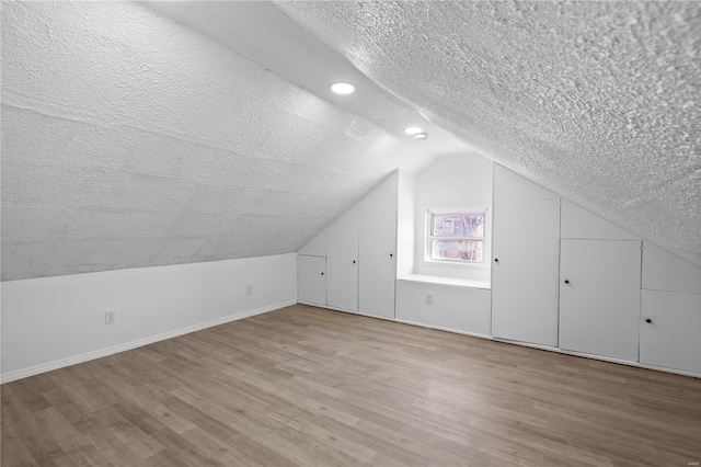 additional living space featuring wood-type flooring, a textured ceiling, and vaulted ceiling