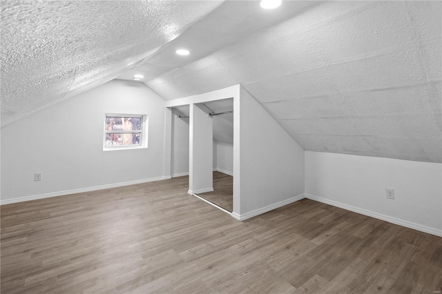 additional living space with hardwood / wood-style floors, a textured ceiling, and vaulted ceiling