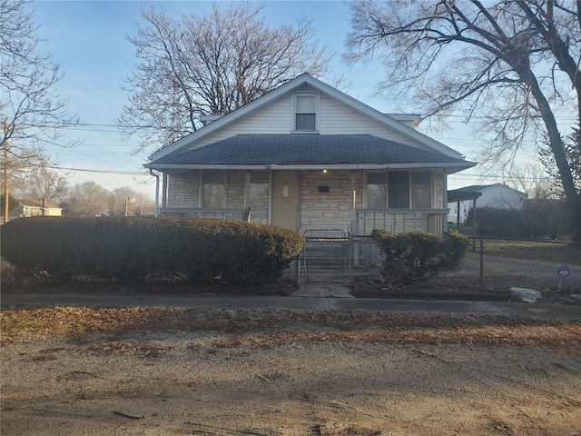 bungalow with stone siding, a fenced front yard, covered porch, and a shingled roof