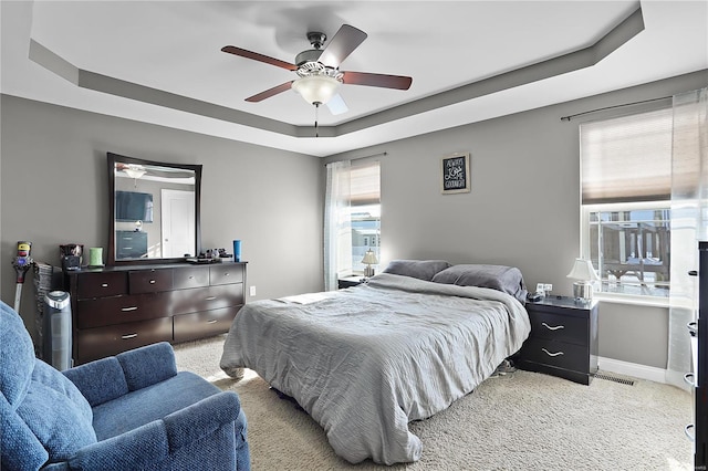 bedroom featuring a raised ceiling, light carpet, and ceiling fan