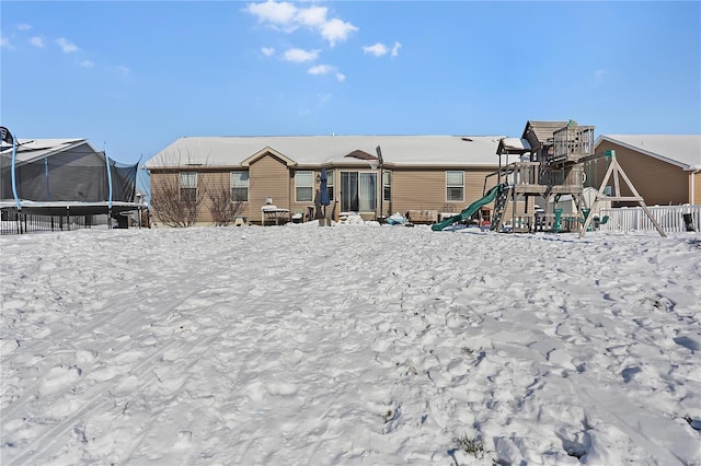 snow covered back of property with a playground and a trampoline