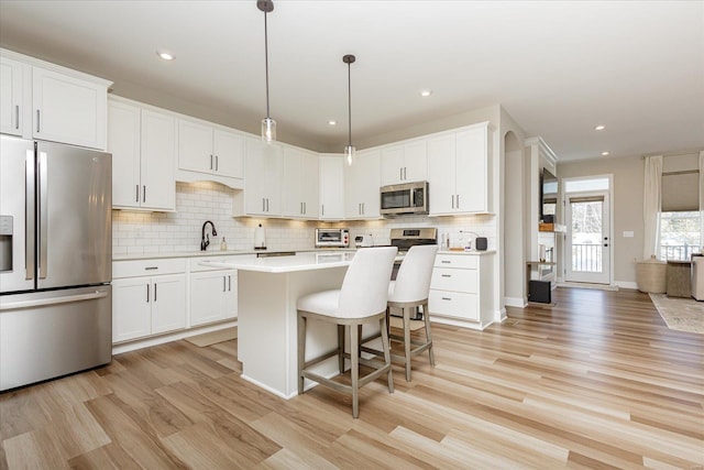 kitchen with white cabinetry, light wood-type flooring, stainless steel appliances, and hanging light fixtures