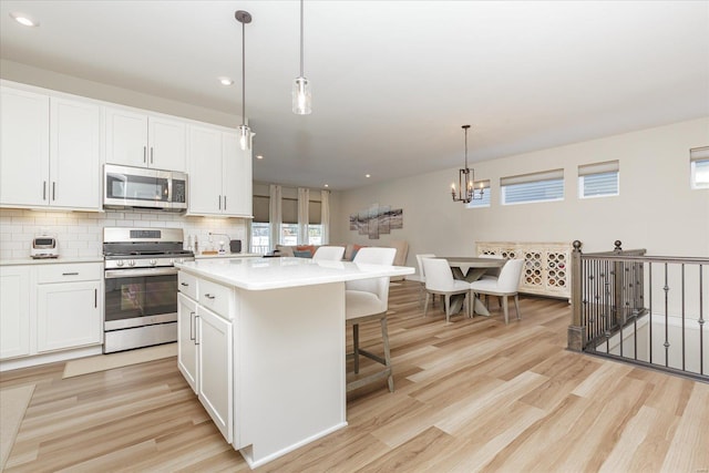 kitchen with decorative light fixtures, backsplash, a kitchen island, stainless steel appliances, and white cabinets