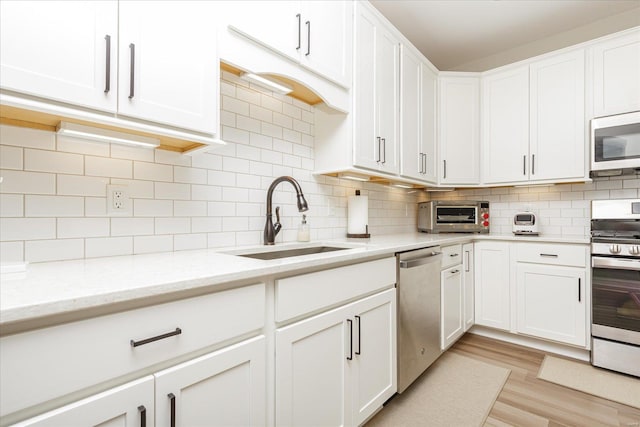 kitchen with appliances with stainless steel finishes, white cabinetry, decorative backsplash, sink, and light stone counters