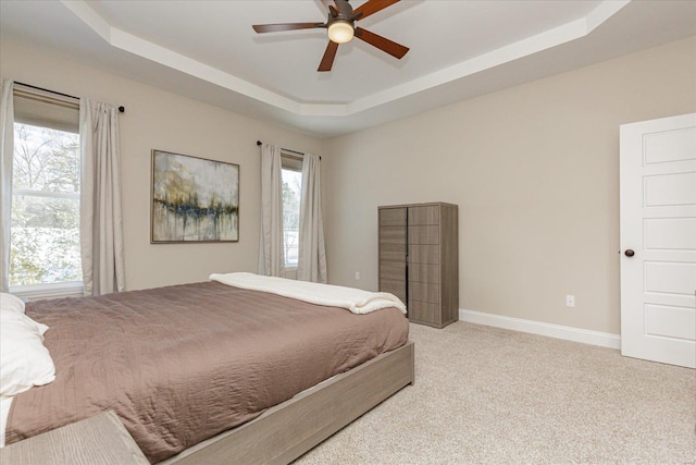 carpeted bedroom with a raised ceiling, ceiling fan, and multiple windows