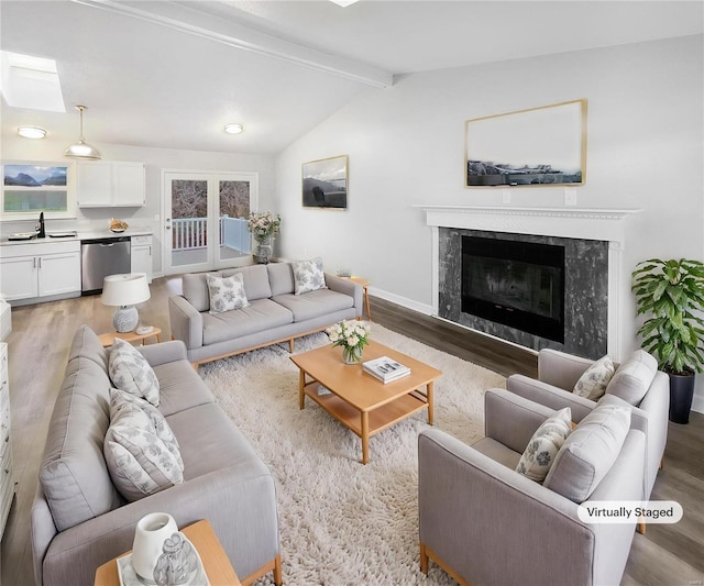 living room featuring hardwood / wood-style flooring, vaulted ceiling with beams, a premium fireplace, and sink