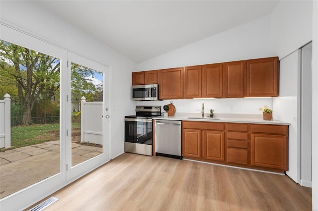 kitchen featuring vaulted ceiling, appliances with stainless steel finishes, sink, and light hardwood / wood-style floors