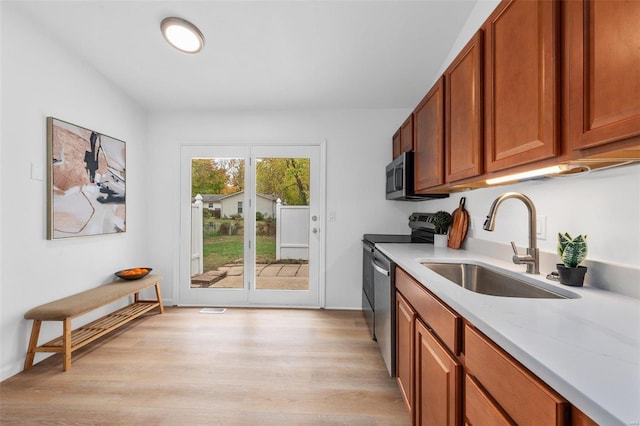 kitchen featuring light stone countertops, sink, stainless steel appliances, and light wood-type flooring