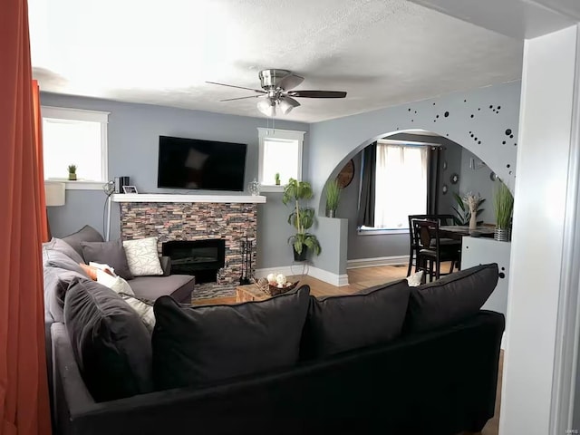 living room with a stone fireplace, ceiling fan, a textured ceiling, and hardwood / wood-style flooring