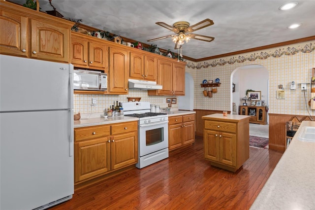 kitchen with tasteful backsplash, white appliances, ceiling fan, crown molding, and dark wood-type flooring