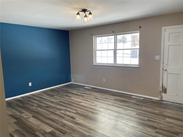 empty room with dark wood-type flooring and an inviting chandelier