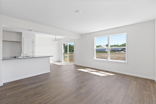 unfurnished living room with a wealth of natural light, sink, dark hardwood / wood-style floors, and an inviting chandelier