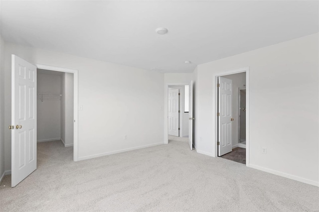 unfurnished bedroom with light carpet, a walk in closet, ensuite bathroom, and a closet