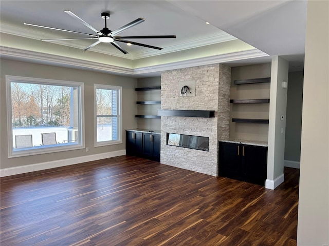 unfurnished living room with crown molding, built in shelves, a fireplace, a tray ceiling, and dark hardwood / wood-style flooring