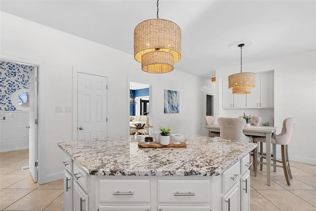 kitchen featuring light tile patterned floors, light stone countertops, a kitchen island, and white cabinets