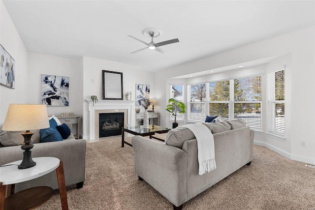 living area featuring baseboards, a fireplace with flush hearth, carpet floors, and ceiling fan