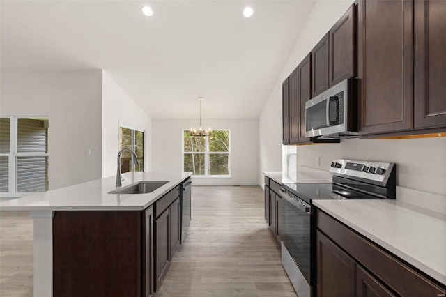 kitchen with appliances with stainless steel finishes, vaulted ceiling, a kitchen island with sink, an inviting chandelier, and hanging light fixtures