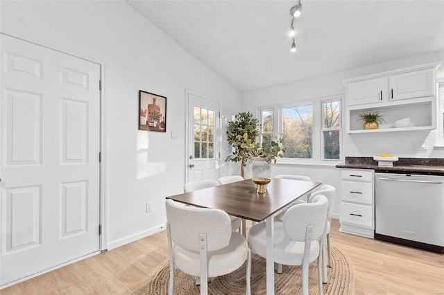 dining space with vaulted ceiling, a textured ceiling, and light hardwood / wood-style flooring