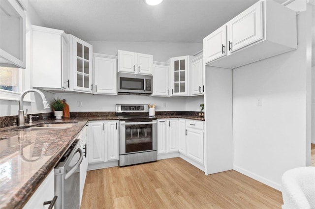 kitchen featuring white cabinetry, appliances with stainless steel finishes, dark stone counters, light hardwood / wood-style flooring, and sink