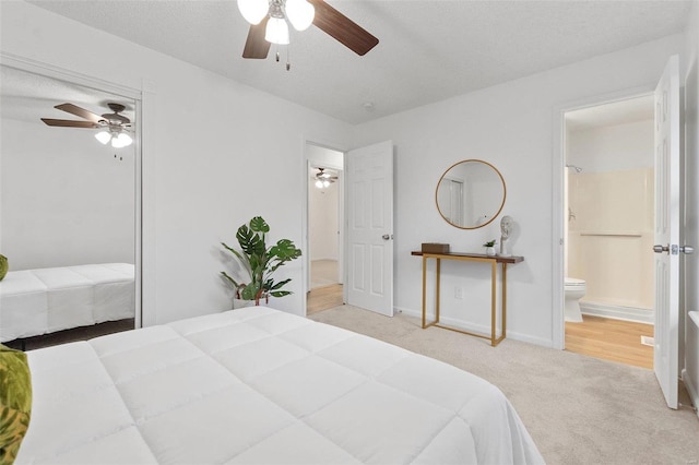 bedroom featuring ceiling fan, a textured ceiling, light carpet, and ensuite bath