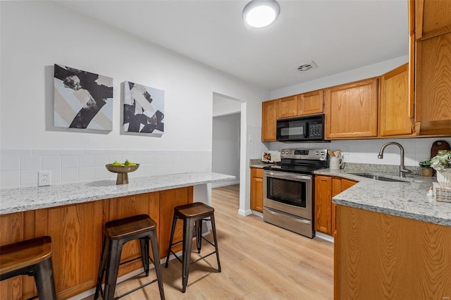 kitchen with light stone countertops, a kitchen breakfast bar, sink, kitchen peninsula, and stainless steel range with electric stovetop